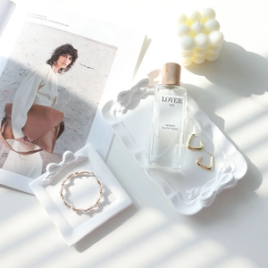 White ceramic bow trays with pearl bracelet, perfume and candle in natural sunlight
