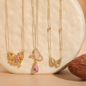 Detail view of three gold butterfly necklaces featuring pink gemstones and shell accents