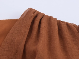 Detailed close-up of caramel brown woven fabric with textured pleats and linen feel