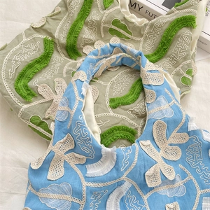 Détail de broderies florales en dentelle 3D et franges sur sacs en toile vert et bleu