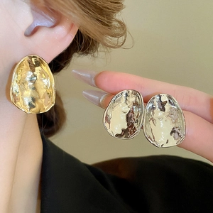 Close-up of model wearing irregular hammered metal earrings in gold and silver