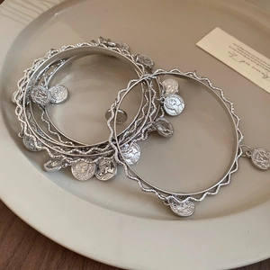 Detail view of silver multi-layer coin pendant bracelet on a minimalist ceramic plate