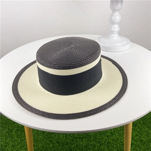 Detailed top view of bicolor straw boater hat with black ribbon on grass background
