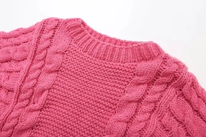 Close-up of pink knit sweater showing round neck and intricate cable knit patterns