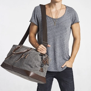 Grey canvas and brown leather travel bag with shoulder strap worn by male model