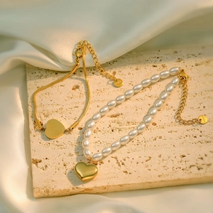 18K gold plated heart pendant bracelet and pearl necklace set on a beige textured stone