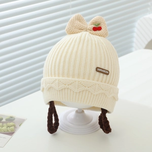 Détail du bonnet tricoté crème pour bébé avec broderie cerise et tresses brunes