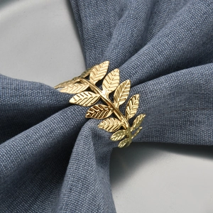 Golden leaf metal napkin ring featuring an intricate leaf design on a blue linen napkin