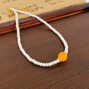 Détail du fermoir plaqué or 18k et des perles blanches sur un fond en bois sombre