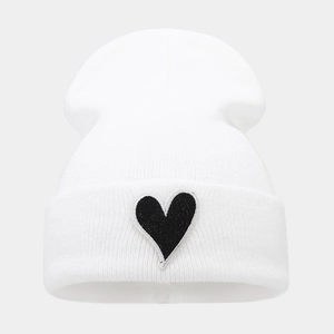 Détail d'un bonnet blanc en maille avec un écusson cœur noir sur le bord à revers