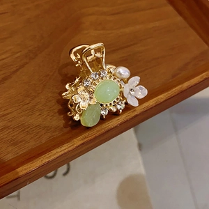 Detailed macro view of golden flower hair claw clip with pearls and green stones
