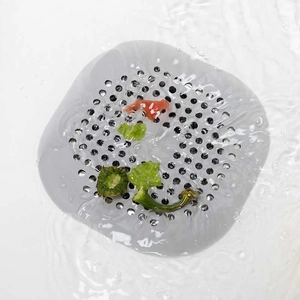 Grey silicone sink strainer with suction cups capturing kitchen debris in a white sink