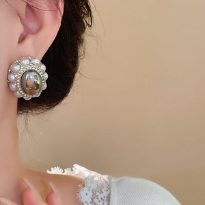 Close-up of vintage style earring with dark gemstone, rhinestones and white pearls on model