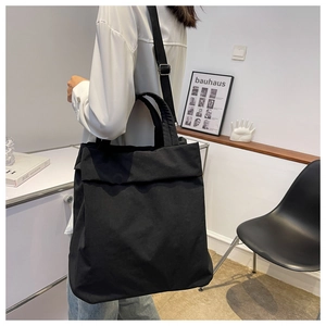 Minimalist black nylon tote bag worn on shoulder by model in modern interior setting