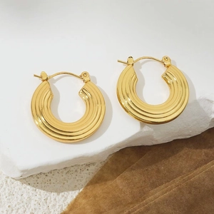 Detail of 18K gold chunky hoop earrings with textured tiered ridges on a stone backdrop