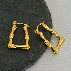 Boucles d'oreilles créoles bambou en acier titane doré sur un plateau en pierre noire