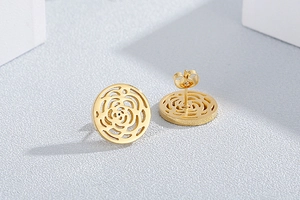 Detailed macro view of golden stainless steel hollow rose stud earrings on grey background