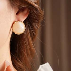Close-up of model wearing vintage round gold-rimmed earrings with beige marble texture