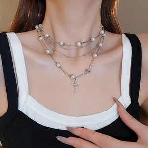 Close-up of a three-layer pearl necklace with a silver cross pendant worn by a model