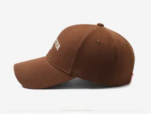 Detail of dark brown cotton baseball cap showing white letter embroidery and twill texture