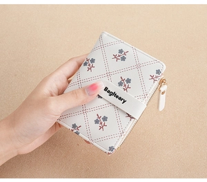 Close-up of a white floral folding wallet with a gold zipper held in hand against fabric