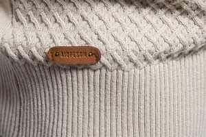 Close-up of beige knit sweater texture featuring ribbed hem and small leather logo patch