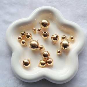 Golden metal bells in various sizes on a white ceramic tray for DIY jewelry and crafts