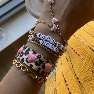 Close-up of stacked gold charm bracelets with leopard print heart and Good Luck charms