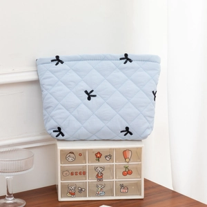 Close-up of light blue quilted cosmetic bag featuring black embroidered bow details