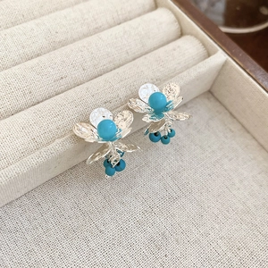 Detailed view of silver flower earrings with blue beads on a beige linen jewelry display