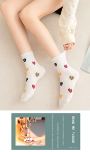 Close-up of white ribbed cotton mid-calf socks featuring colorful heart patterns on model