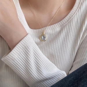 Close-up of a two-tone gold and silver coin pendant necklace worn by a model