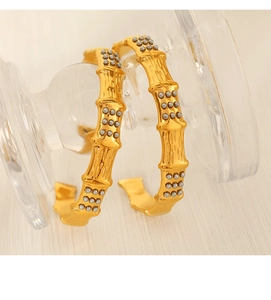 Close-up of golden bamboo style hoop earrings with grey beads on a glass stand
