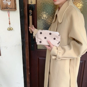 Macro shot of retro corduroy makeup bag with brown dots held by a model in a cozy cafe