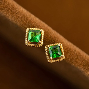 Classic gold square stud earrings with green zircon stones on brown fabric background