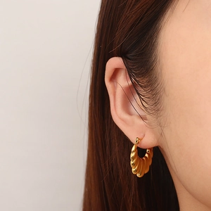 Gros plan de boucles d'oreilles créoles dorées en U avec texture nervurée sur modèle