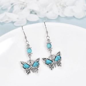 Bohemian silver butterfly earrings with turquoise inlay displayed on a white plate
