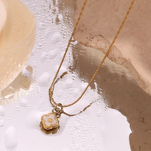 Detailed view of an 18K gold flower pendant with white shell inlay on a wet mirror surface