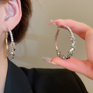 Close-up of sparkling silver geometric hoop earrings with crystals on a female model
