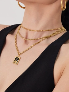 Detail of layered gold necklaces with a rectangular vintage pendant and white pearl inlay