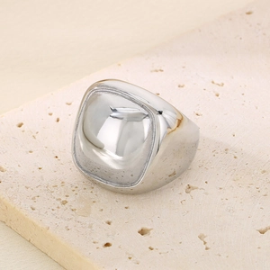 Macro shot of chunky silver square stainless steel ring on beige stone texture