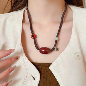 Detail of vintage beaded necklace featuring a large red agate and metal blessing charm