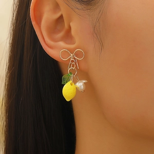 Close-up of yellow lemon drop earring with golden bow and pearl detail on ear