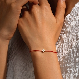 Detail of red string bracelet with gold clover charm and inlaid white crystals