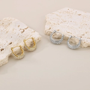 Detailed view of luxury gold and silver C-shaped rhinestone hoop earrings on stone