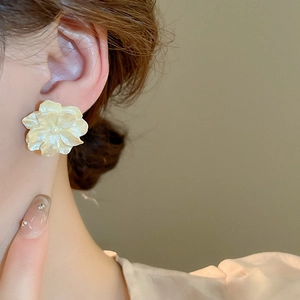 Close-up of matte camellia flower earrings in cream yellow on a model ear