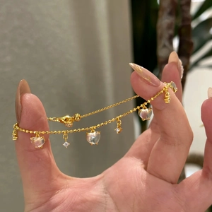 Detailed close-up of golden heart tassel bracelet with opal-like stones and crystals