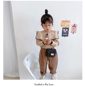 Toddler girl wearing khaki shirt, brown pants and black tweed chain mini crossbody bag