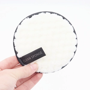 Close-up of white plush facial cleansing sponge with black piping and clean sponge label