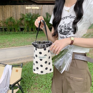 Mini polka dot canvas bucket bag with drawstring closure held in a scenic outdoor setting